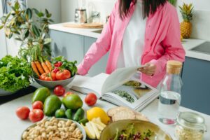 dietista che consulta libro di nutrizione e ha davanti degli alimenti